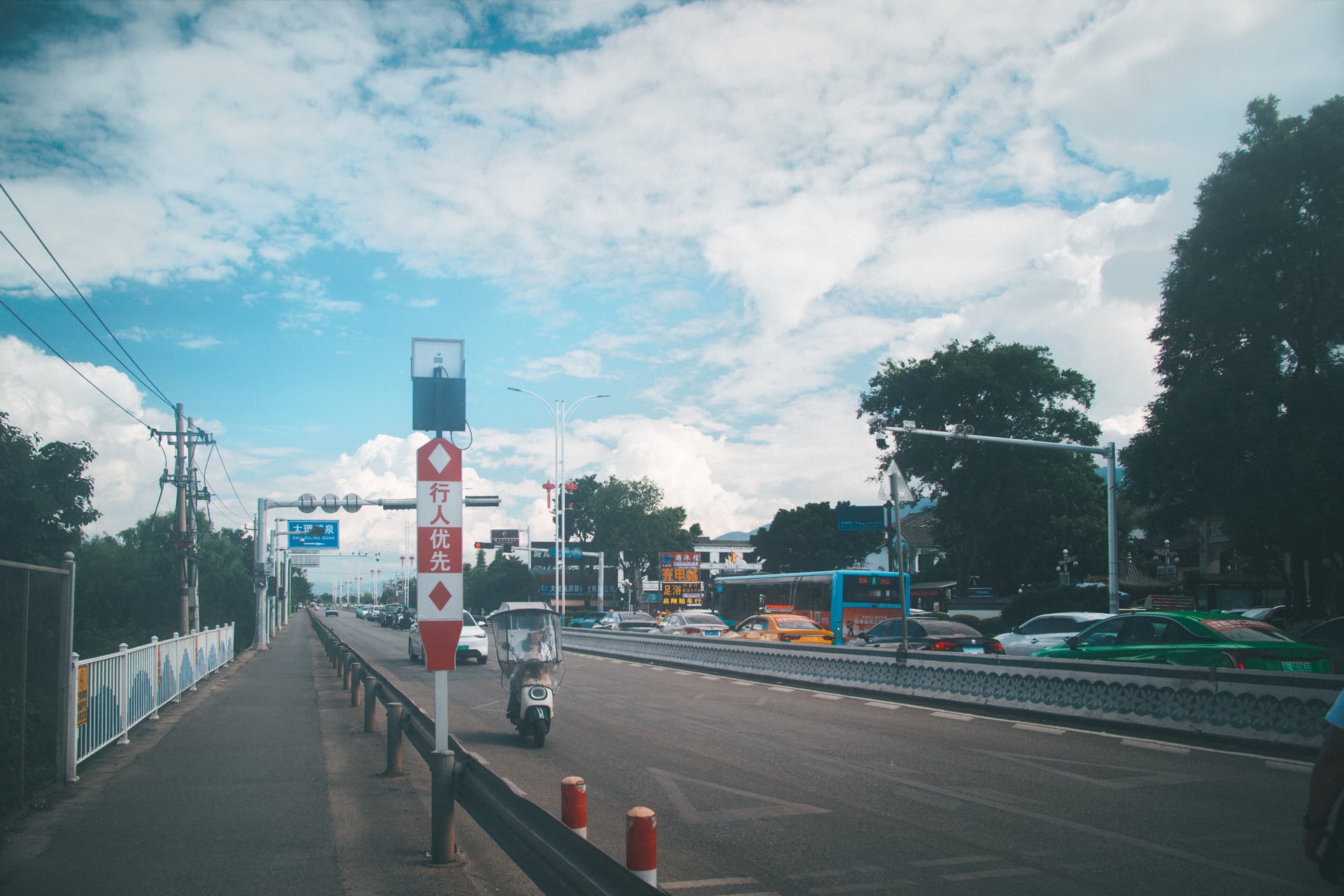 蓝天下通往大理之泉的道路上，车辆与行人交错经过。