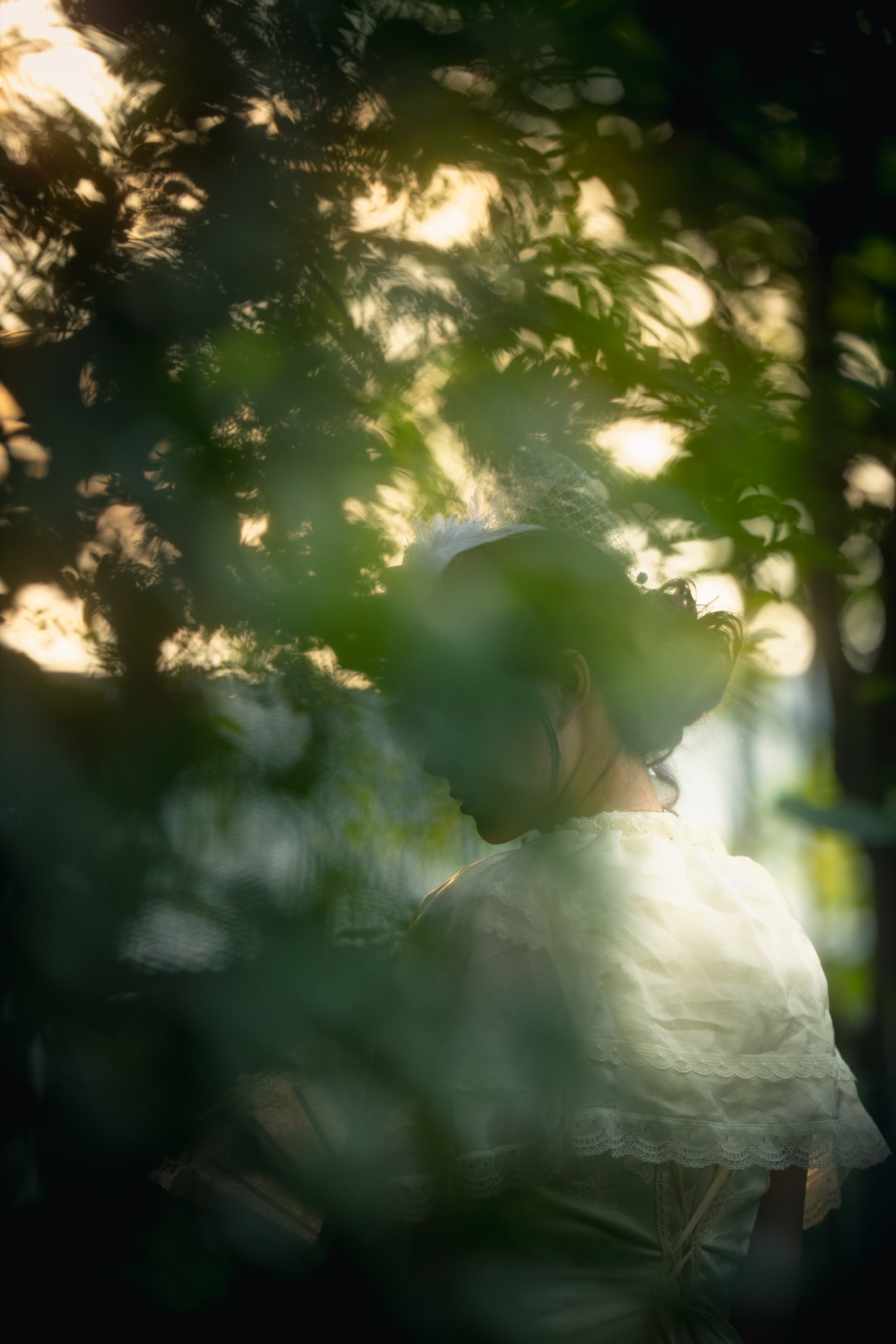 枝叶遮挡下，一名穿白衣的女子低头侧身站立。