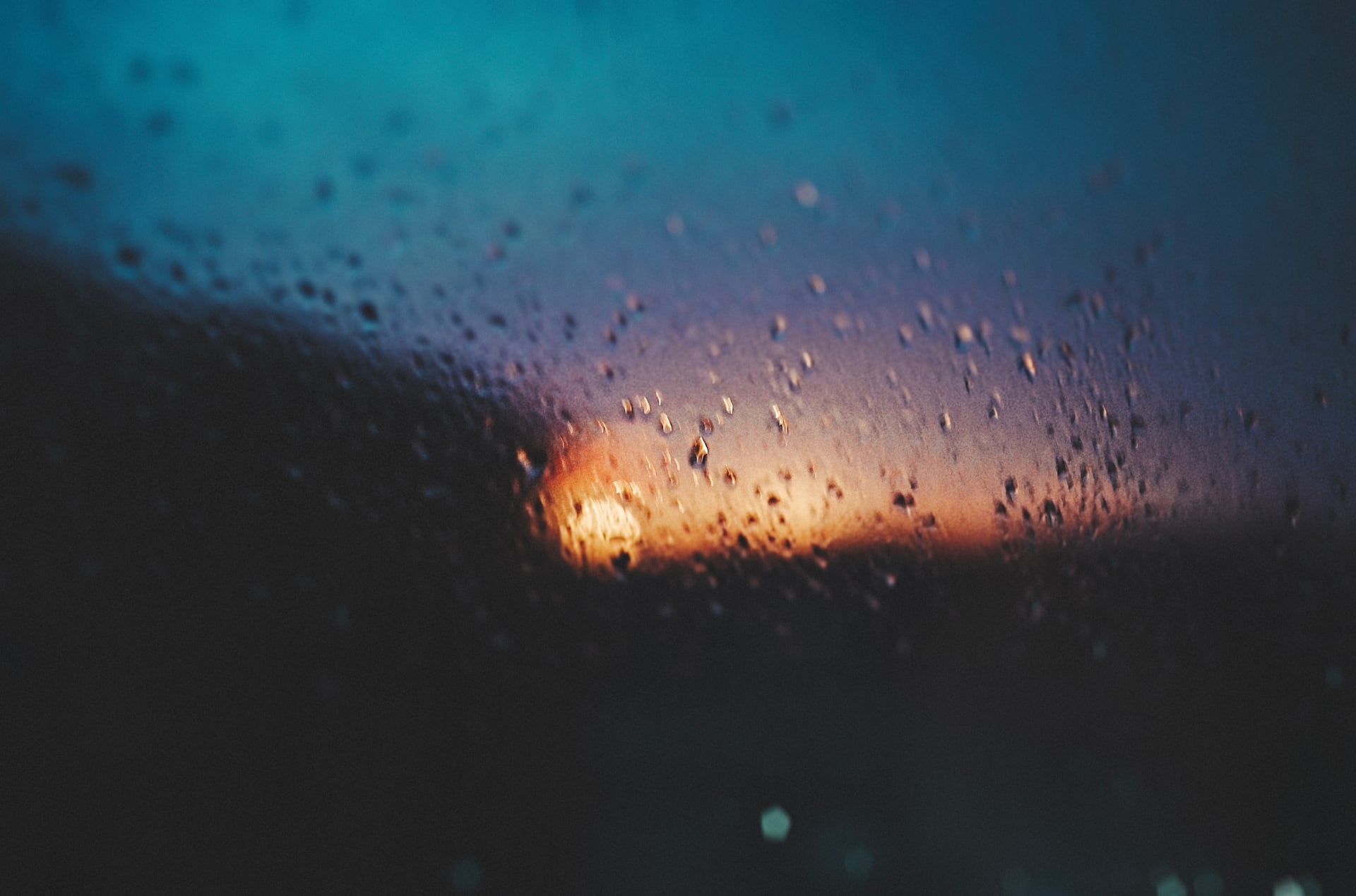 雨滴凝在玻璃上，后方橙蓝灯光模糊成色块。